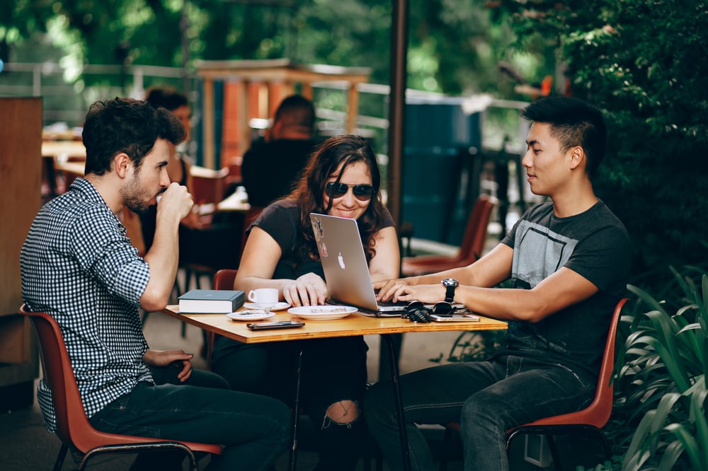 Three young adults drinking coffee and looking at a laptop screen