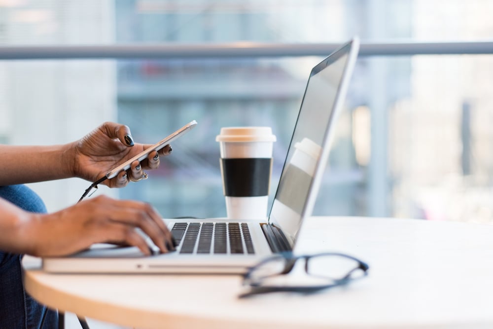 Image of woman's hands. One hand is texting and the other is typing on laptop.