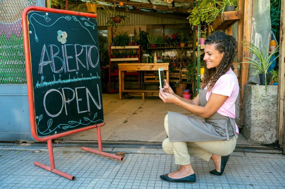 Woman taking photo of open sign outside her shop