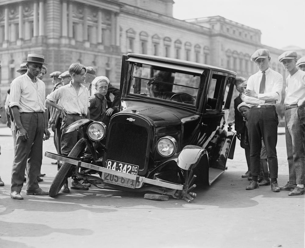 Photo from 1920s of men and boys standing around car with front wheel broken off