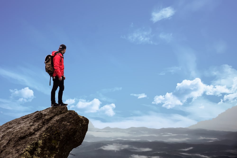 Mountain climber looking into distance on edge of rock