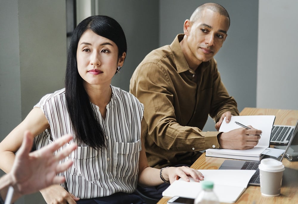 Young woman and man listening to someone speak during business meeting