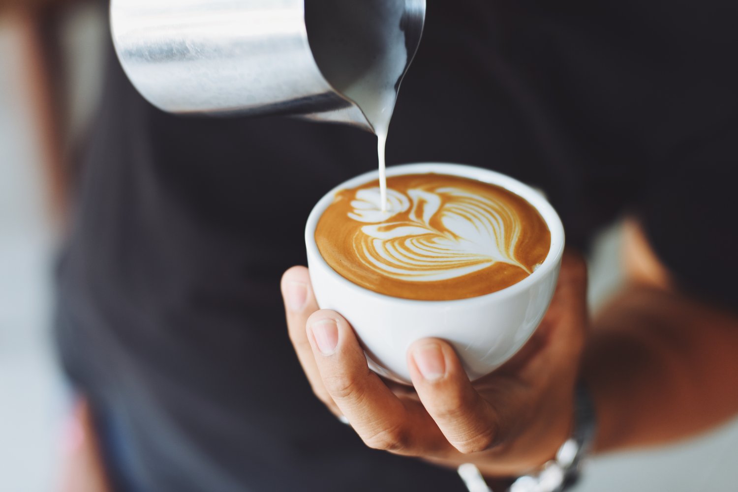 Close up of barista pouring cappuccino with flower pattern on top