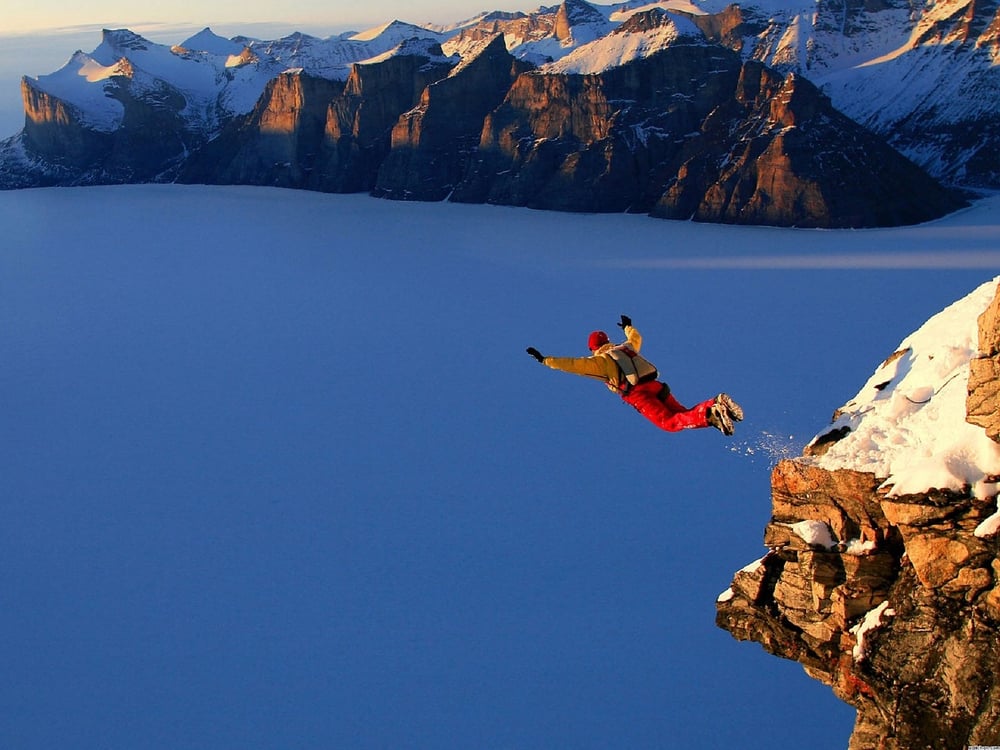 Base jumper leaping from a snowy cliff
